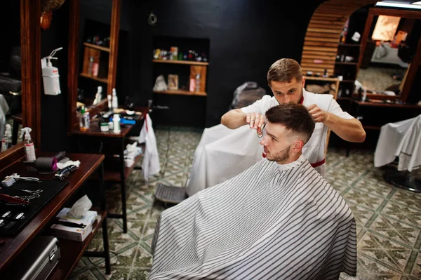 Young bearded man getting haircut by hairdresser while sitting i ...
