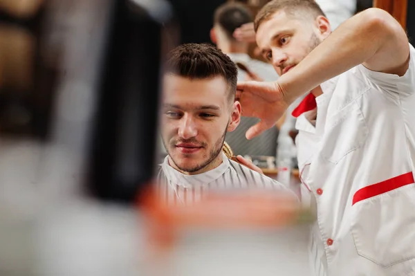 Young bearded man getting haircut by hairdresser while sitting i