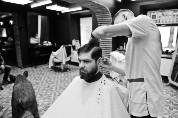 Jeune homme barbu se faire couper les cheveux par coiffeur tout en étant assis i — Photo