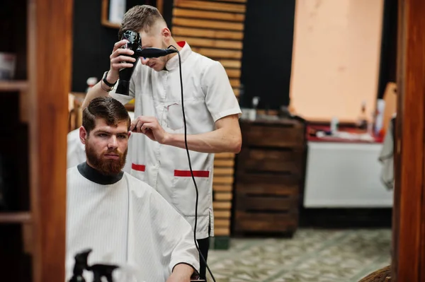 Young bearded man getting haircut by hairdresser while sitting i