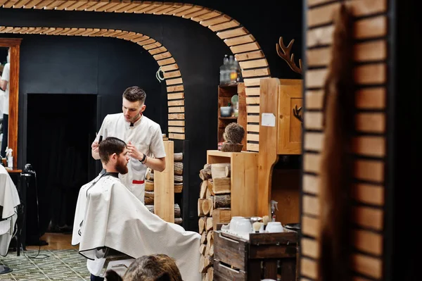 Young bearded man getting haircut by hairdresser while sitting i