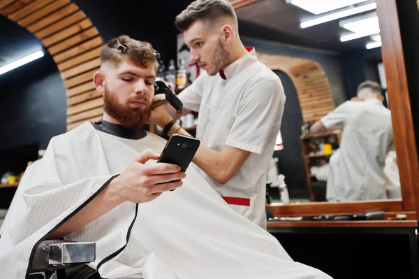 Jeune homme barbu se faire couper les cheveux par coiffeur tout en étant assis i — Photo