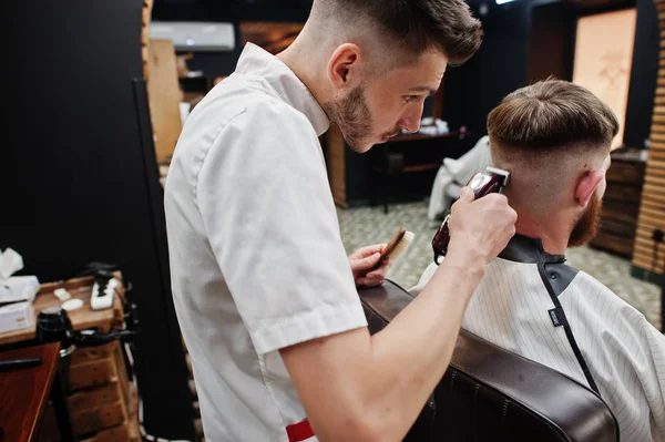 Jeune homme barbu se faire couper les cheveux par coiffeur tout en étant assis i — Photo