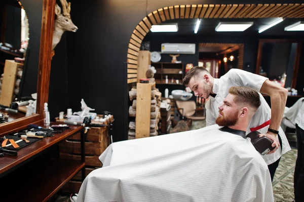 Young bearded man getting haircut by hairdresser while sitting i