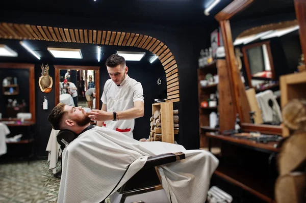 Young bearded man getting haircut by hairdresser while sitting i