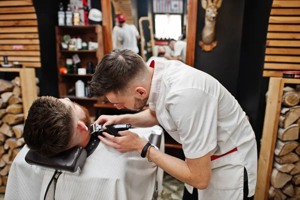 Young bearded man getting haircut by hairdresser while sitting i — Stock Photo, Image