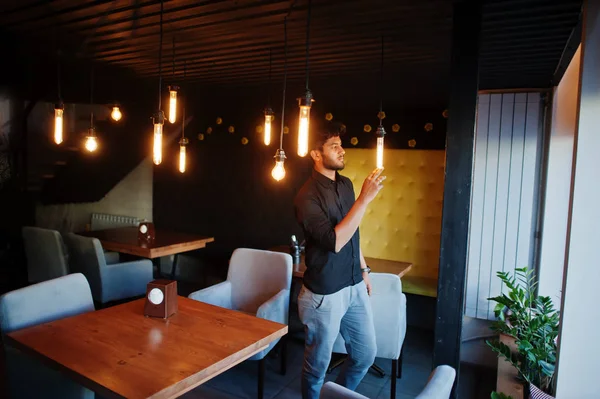 Уверенный молодой индиец в черной рубашке, стоящий в кафе . — стоковое фото