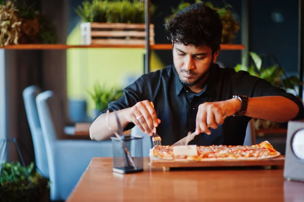 Selbstbewusster junger indischer Mann im schwarzen Hemd sitzt in der Pizzeria wi — Stockfoto