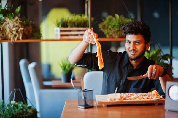 Confiant jeune homme indien en chemise noire assis à la pizzeria wi — Photo