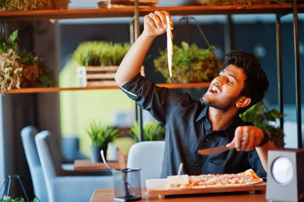 Selbstbewusster junger indischer Mann im schwarzen Hemd sitzt in der Pizzeria wi — Stockfoto