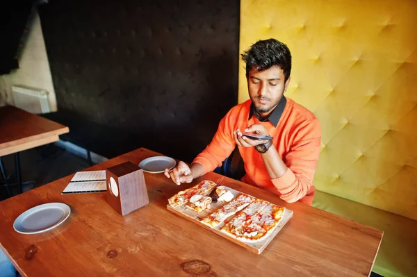 Confiant jeune homme indien en pull orange assis à la pizzeria — Photo