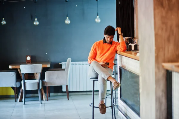 자신감 있는 젊은 인도 남자 에 오렌지 스웨터 앉아 바 카운터 — 스톡 사진