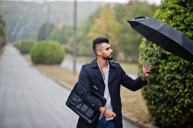 Modaya uygun uzun Arap sakallı adam şemsiyeli siyah bir ceket giyiyor.