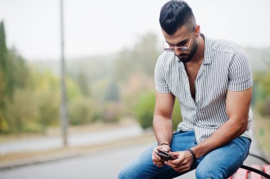 Modaya uygun uzun sakallı adam gömlek, kot pantolon ve güneş gözlüğü giyiyor.