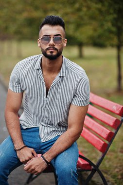 Modaya uygun uzun sakallı adam gömlek, kot pantolon ve güneş gözlüğü giyiyor.