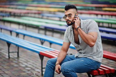 Modaya uygun uzun sakallı adam gömlek, kot pantolon ve güneş gözlüğü giyiyor.