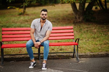 Modaya uygun uzun sakallı adam gömlek, kot pantolon ve güneş gözlüğü giyiyor.