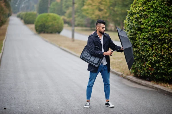 Modaya uygun uzun Arap sakallı adam şemsiyeli siyah bir ceket giyiyor.