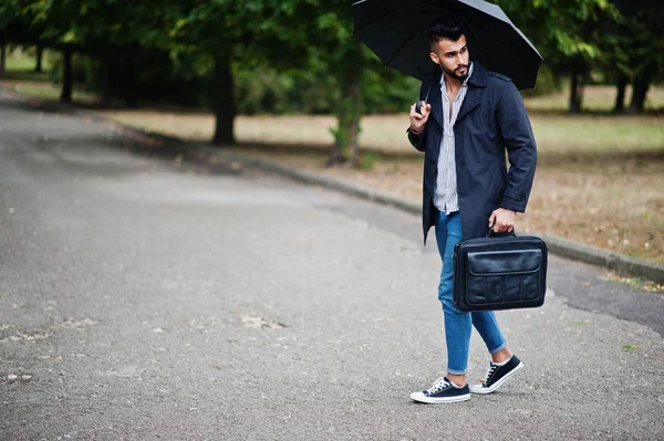 Modaya uygun uzun Arap sakallı adam şemsiyeli siyah bir ceket giyiyor.