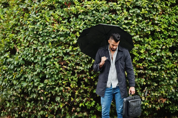 Modaya uygun uzun Arap sakallı adam şemsiyeli siyah bir ceket giyiyor.