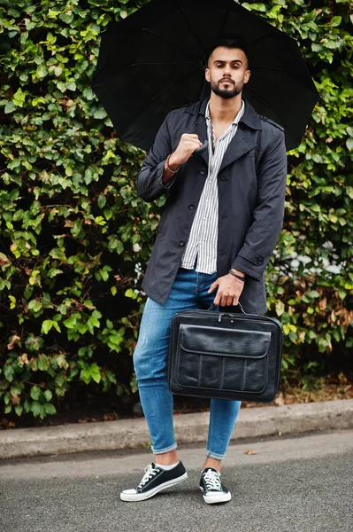 Modaya uygun uzun Arap sakallı adam şemsiyeli siyah bir ceket giyiyor.