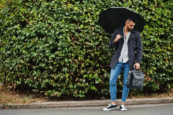 Modaya uygun uzun Arap sakallı adam şemsiyeli siyah bir ceket giyiyor.