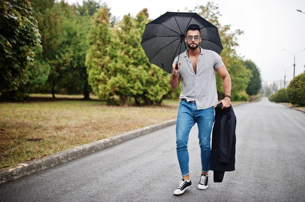 Modaya uygun uzun sakallı adam gömlek, kot pantolon ve güneş gözlüğü giyiyor.