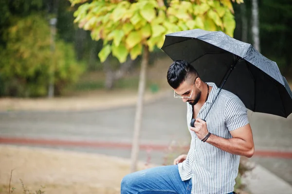 Modaya uygun uzun sakallı adam gömlek, kot pantolon ve güneş gözlüğü giyiyor.