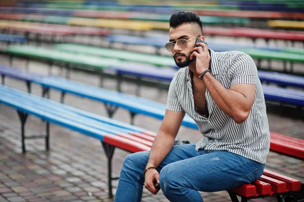 Modaya uygun uzun sakallı adam gömlek, kot pantolon ve güneş gözlüğü giyiyor.