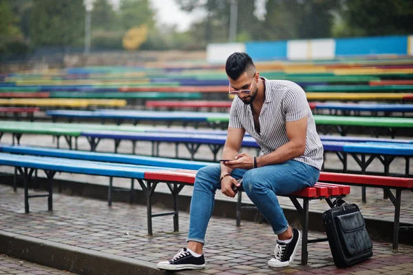 Modaya uygun uzun sakallı adam gömlek, kot pantolon ve güneş gözlüğü giyiyor.