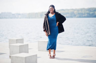 Afro-amerikan esmer tenli artı boyut modeli mavi bir şey poz vermiş.