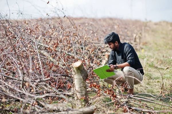 South asian agronomist farmer with clipboard inspecting cut tree