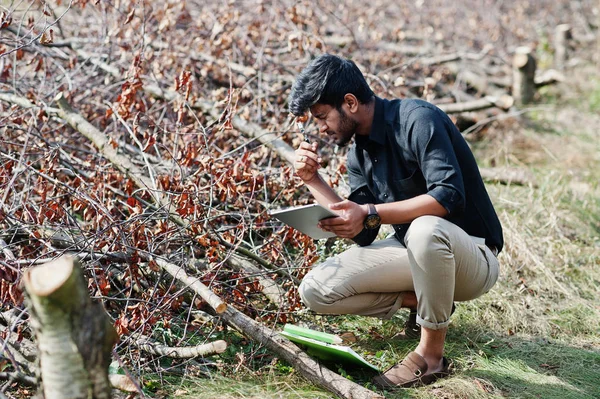 South asian agronomist farmer with clipboard inspecting cut tree