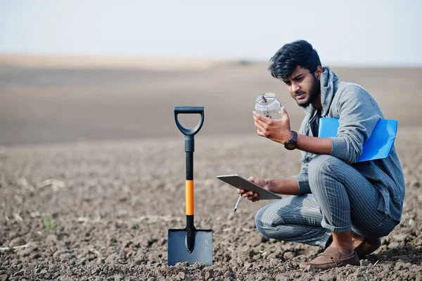 South asian agronomist farmer with shovel inspecting black soil.