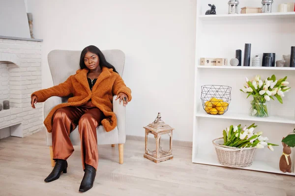 Elegante mujer afroamericana en abrigo naranja posado en la habitación sitt — Foto de Stock