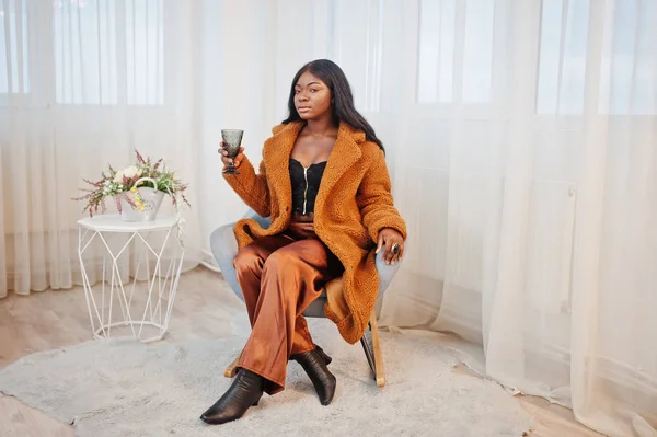 Elegante mujer afroamericana en abrigo naranja posado en la habitación sitt — Foto de Stock