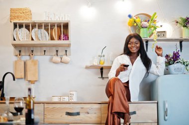 Afro-Amerikalı kadın, romantik evinde mutfakta şarap içiyor.