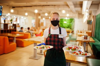 Koruyucu maskeli garson restoranda salata tabağı tutuyor..
