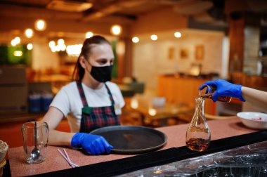 Koruyucu maske takan garson restoranda alkollü içecek tepsisiyle bekliyor..