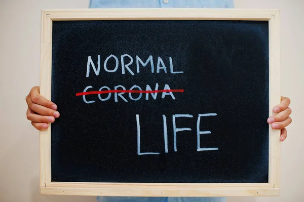 Normal or Corona life? Coronavirus concept. Boy hold inscription on the board.