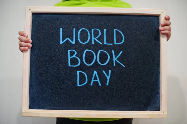 World book day. Boy hold chalkboard with blue inscription.