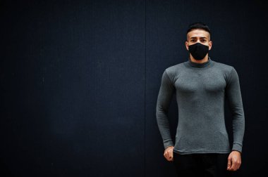 Gri balıkçı yakalı ve siyah yüzlü Ortadoğulu adam soyutlanmış arka planda maske takıyor..