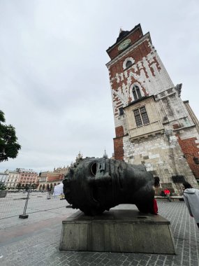 Krakow, Polonya - 08 Temmuz 2025: Krakow, Polonya 'da bulutlu gökyüzünün altında saat kulesinin yakınındaki tarihi meydanda bronz heykel. 