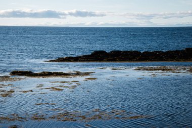 Huzurlu kıyı manzarası kayalık oluşumlar, yumuşak okyanus dalgaları ve sakin bir atmosfer içerir..