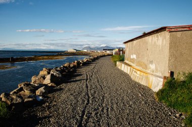 İzlanda 'da açık mavi gökyüzünün altında kayalık bir kıyı şeridi yakınında çakıl yolu.