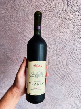 Kyiv, Ukrayna - 10 Ağustos 2025: Plantaze Vranac şarap şişesini sanatsal ve desenli arka planda tutan kişi