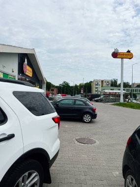 Chelm, Polonya - 10 Ağustos 2025: Biedronka ticari alanına park edilmiş araçlar ve yakındaki bir market ve bulutlu gökyüzü.