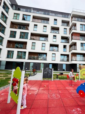 Modern bir apartmanın yanındaki renkli oyun parkında eğlenen çocuklar..