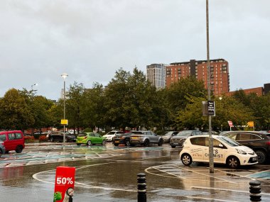 Manchester, İngiltere - 10 Eylül 2025: Araçlar Manchester 'da ıslak bir otoparka park edilmiş kentsel binalar ve yeşillikler.