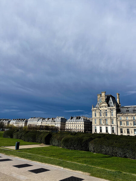 Париж, Франция - 31 марта 2024 года: Историческая архитектура Лувра в окружении зелени под облачным небом в Париже, Франция.